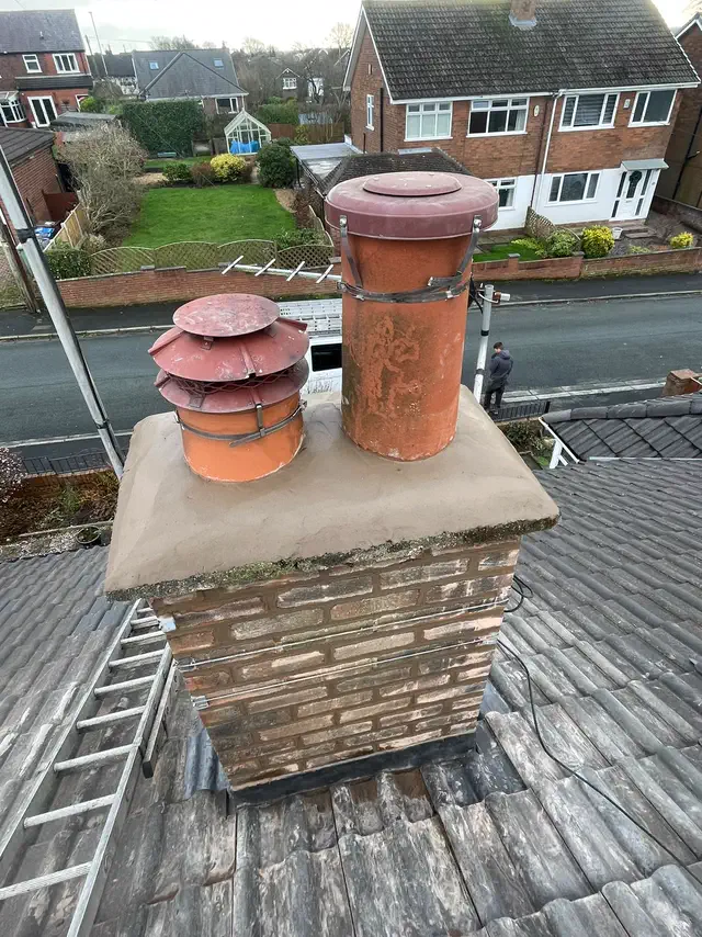 A brick chimney stack with clay pots and a cowl, seen from the roof